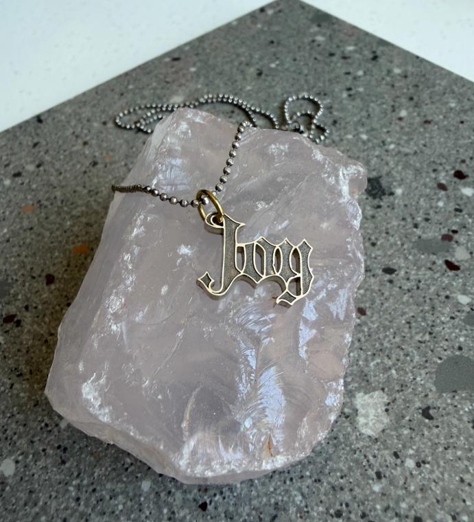 A small pendant that reads "JOY" in a gothic typeface.