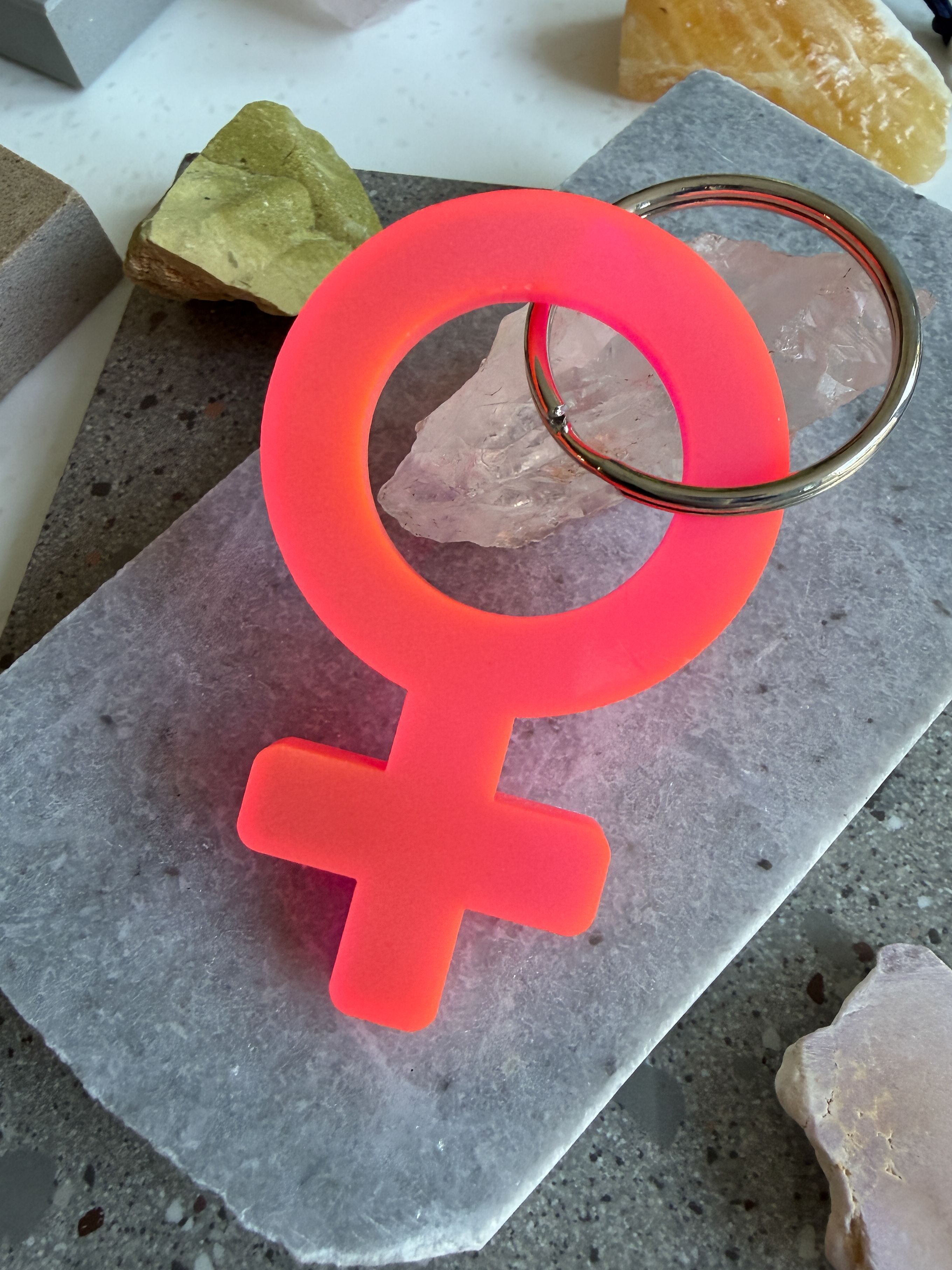 A neon pink acrylic Woman symbol keychain