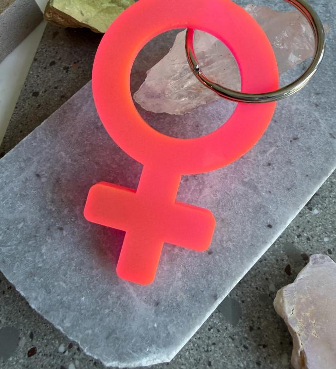 A neon pink acrylic Woman symbol keychain