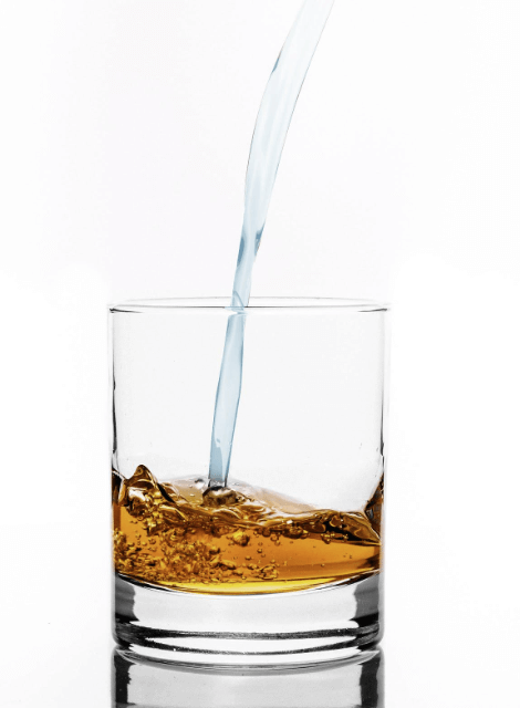 Water pouring into glass with whiskey