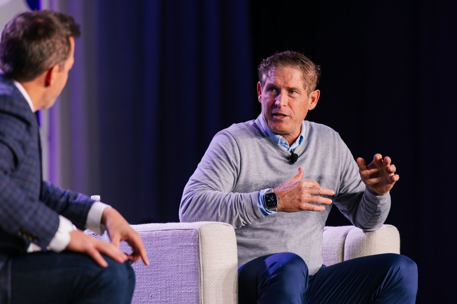 Two men in casual business attire engaged in a panel discussion on stage.