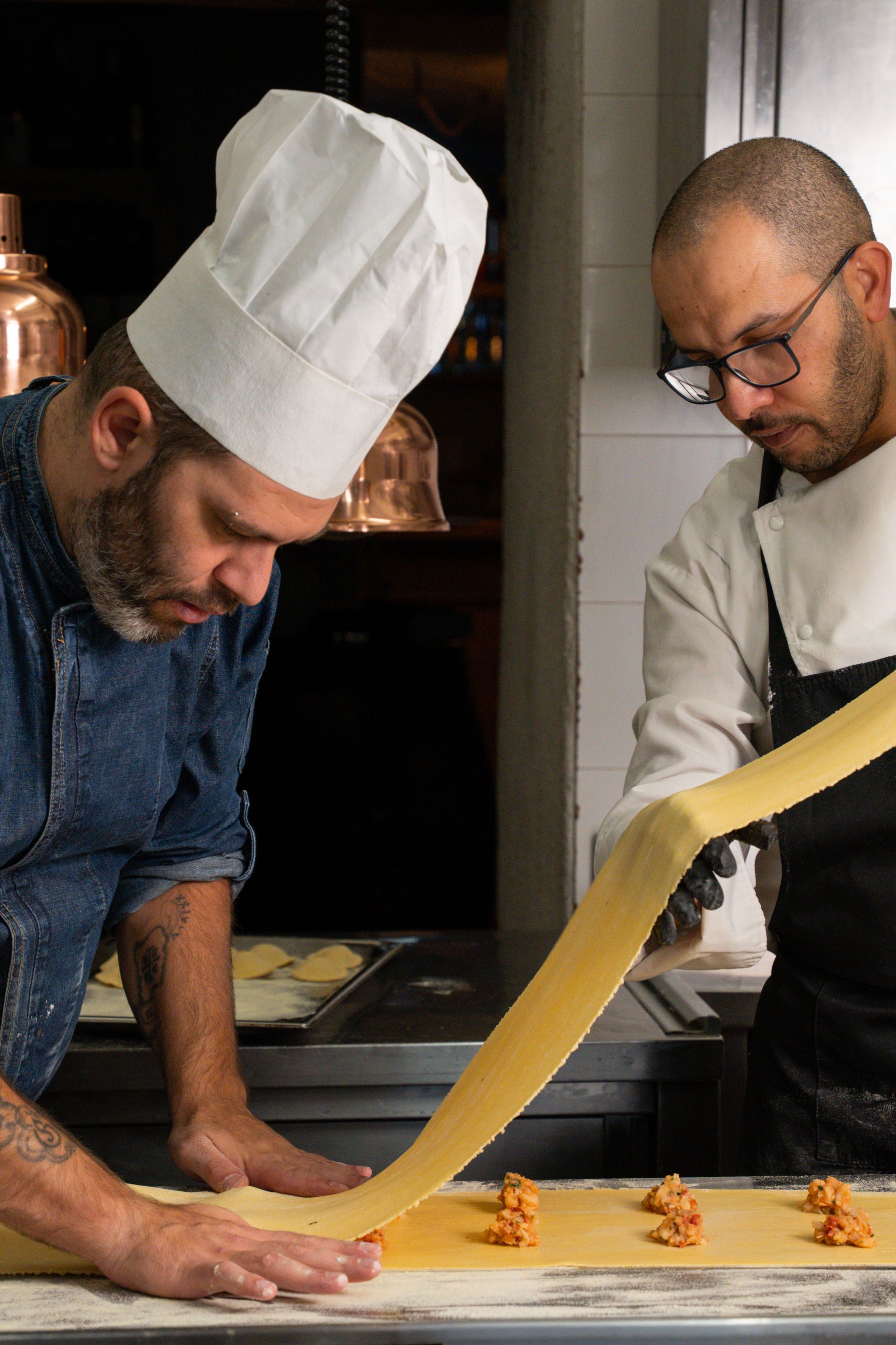 Due cuochi intenti a preparare pasta fresca ripiena piegando la sfoglia sulla farcia in cucina.