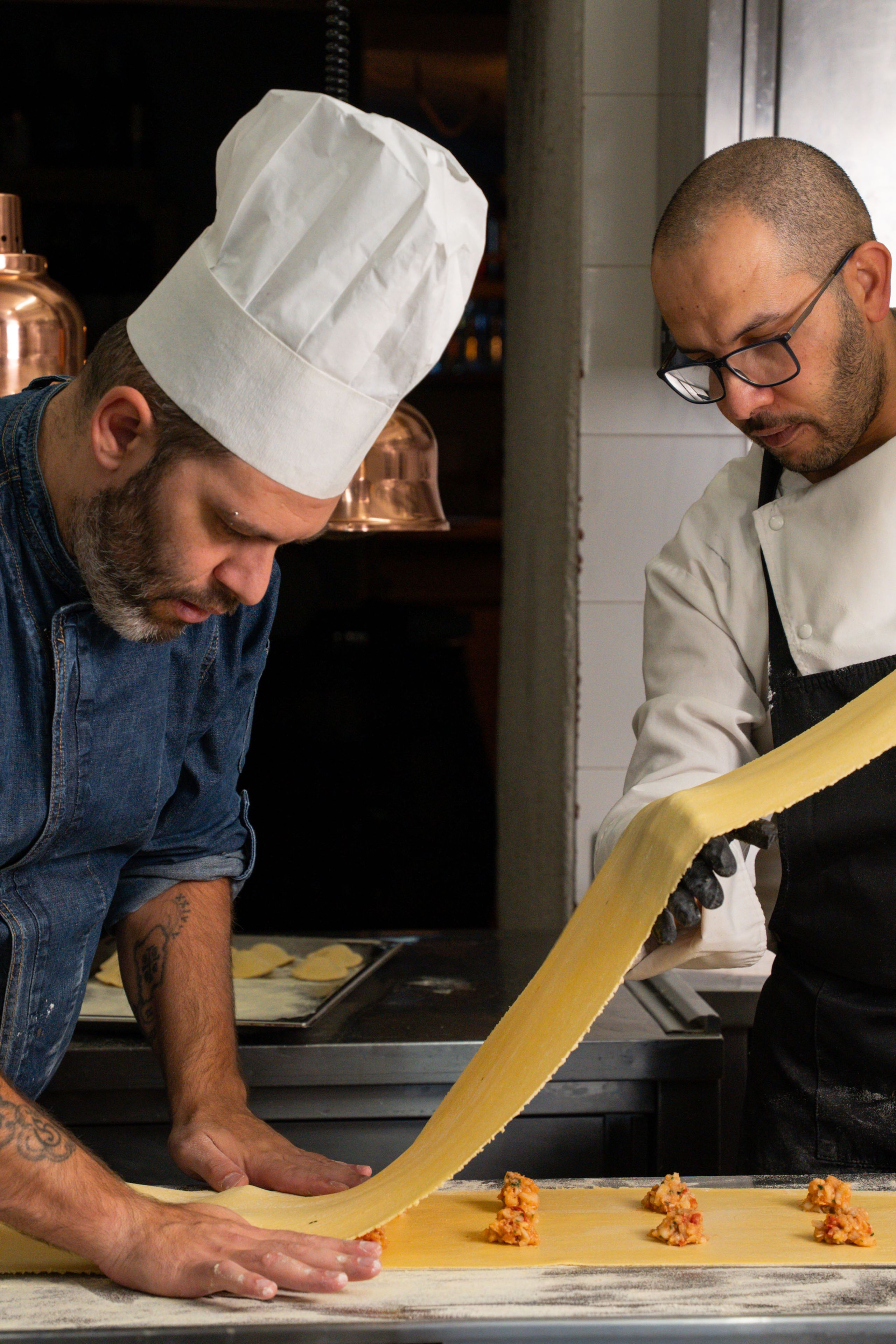 Due cuochi intenti a preparare pasta fresca ripiena piegando la sfoglia sulla farcia in cucina.