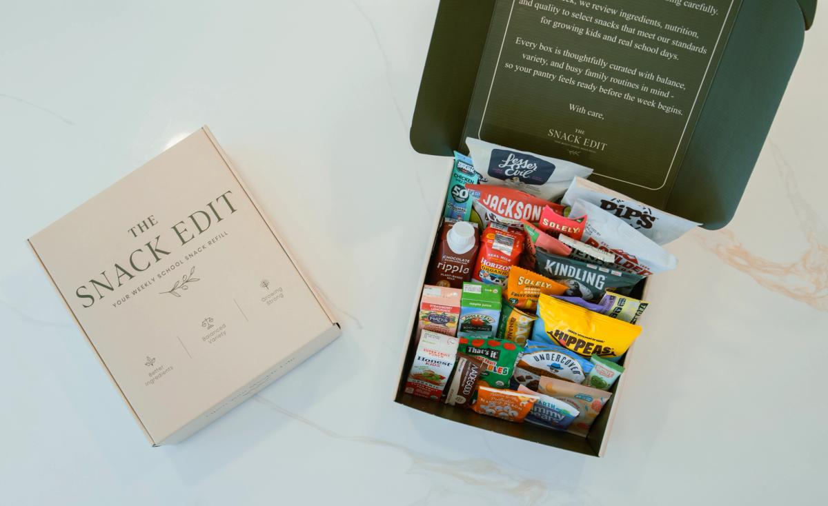 Open and closed The Snack Edit school snack boxes with packaged snacks and small drinks