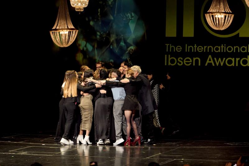 Gruppe som klemmer hverandre på scenen med lysekroner og IIA-logo