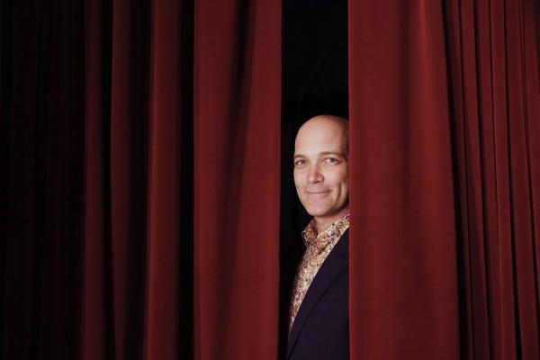 Taylor Mac peeking through theater curtains