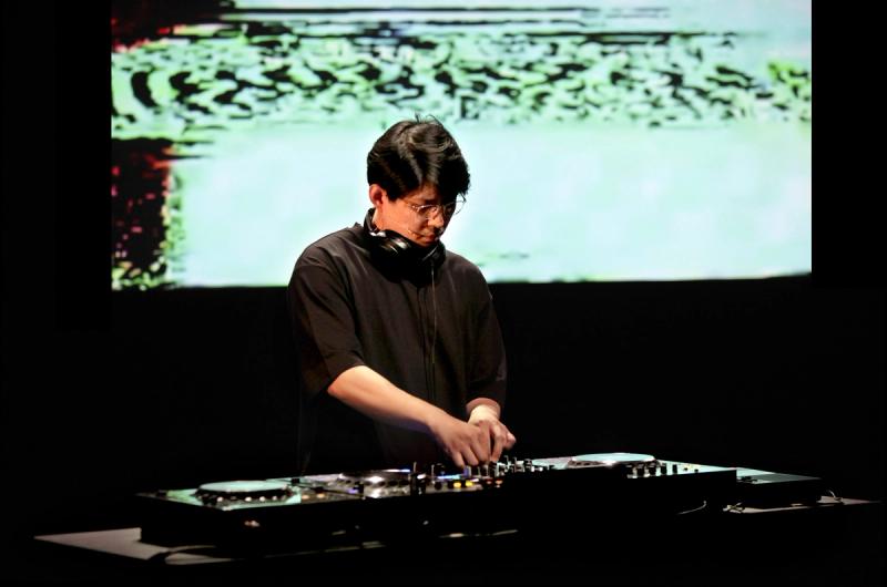 Man by DJ table with a colorful screen in the background