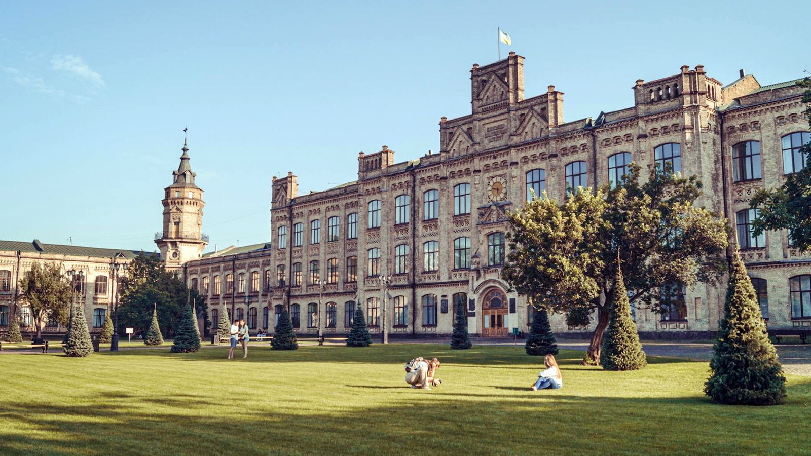 A historic university building overlooking a manicured campus lawn where students relax.