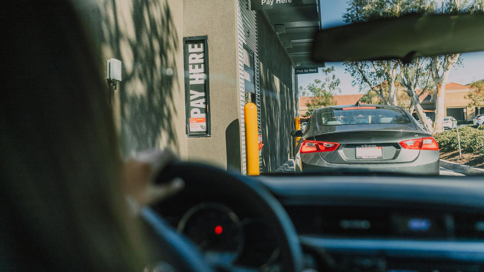 View from inside a car in a quick-service restaurant drive-thru lane approaching a 'Pay Here' window.
