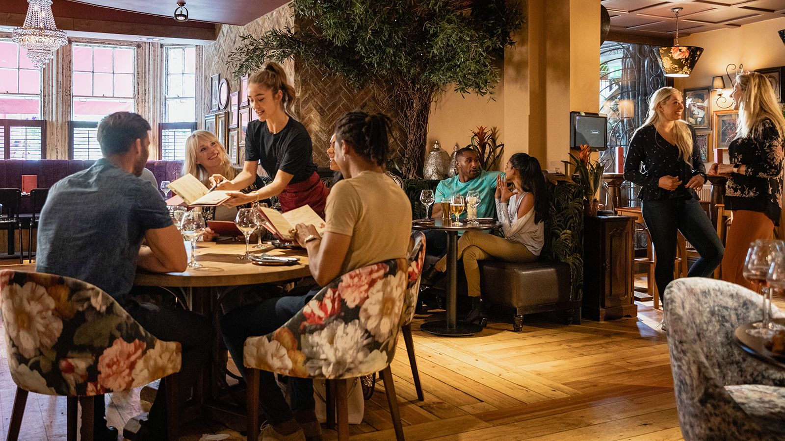 A server presents a menu to seated guests in a warm, full-service restaurant dining room.