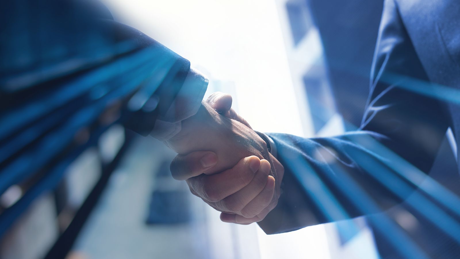 Two businesspeople shaking hands, overlaid with a blue double-exposure of office towers.