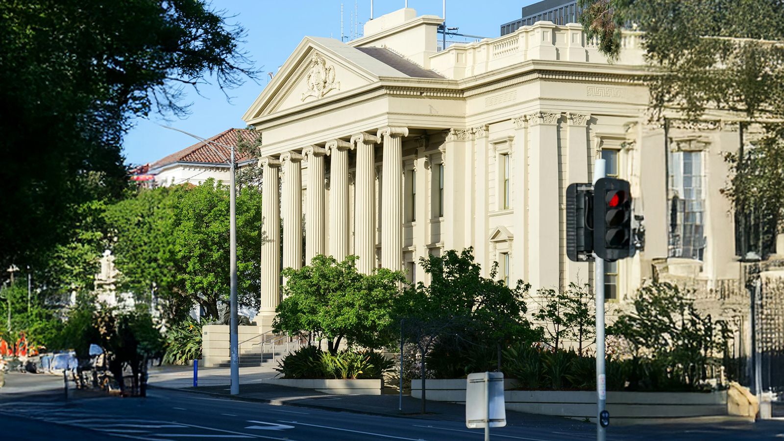 A neoclassical government building with stone columns on a quiet city street under a clear sky.