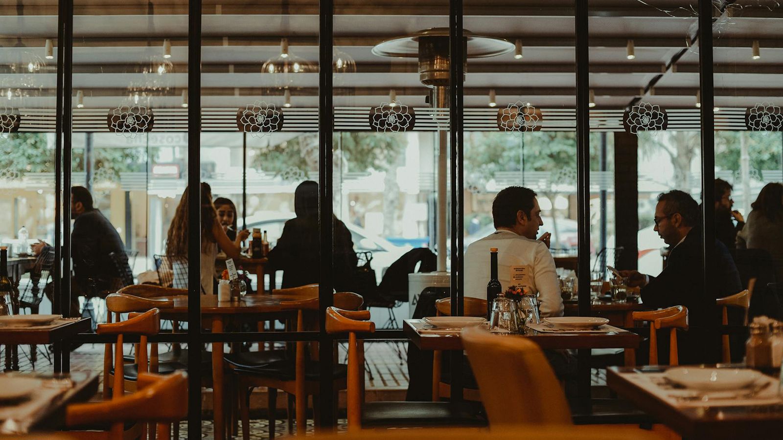 Diners seated at tables inside a contemporary full-service restaurant, viewed through a glass partition.