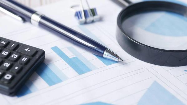 A magnifying glass, calculator, and pen over printed financial documents