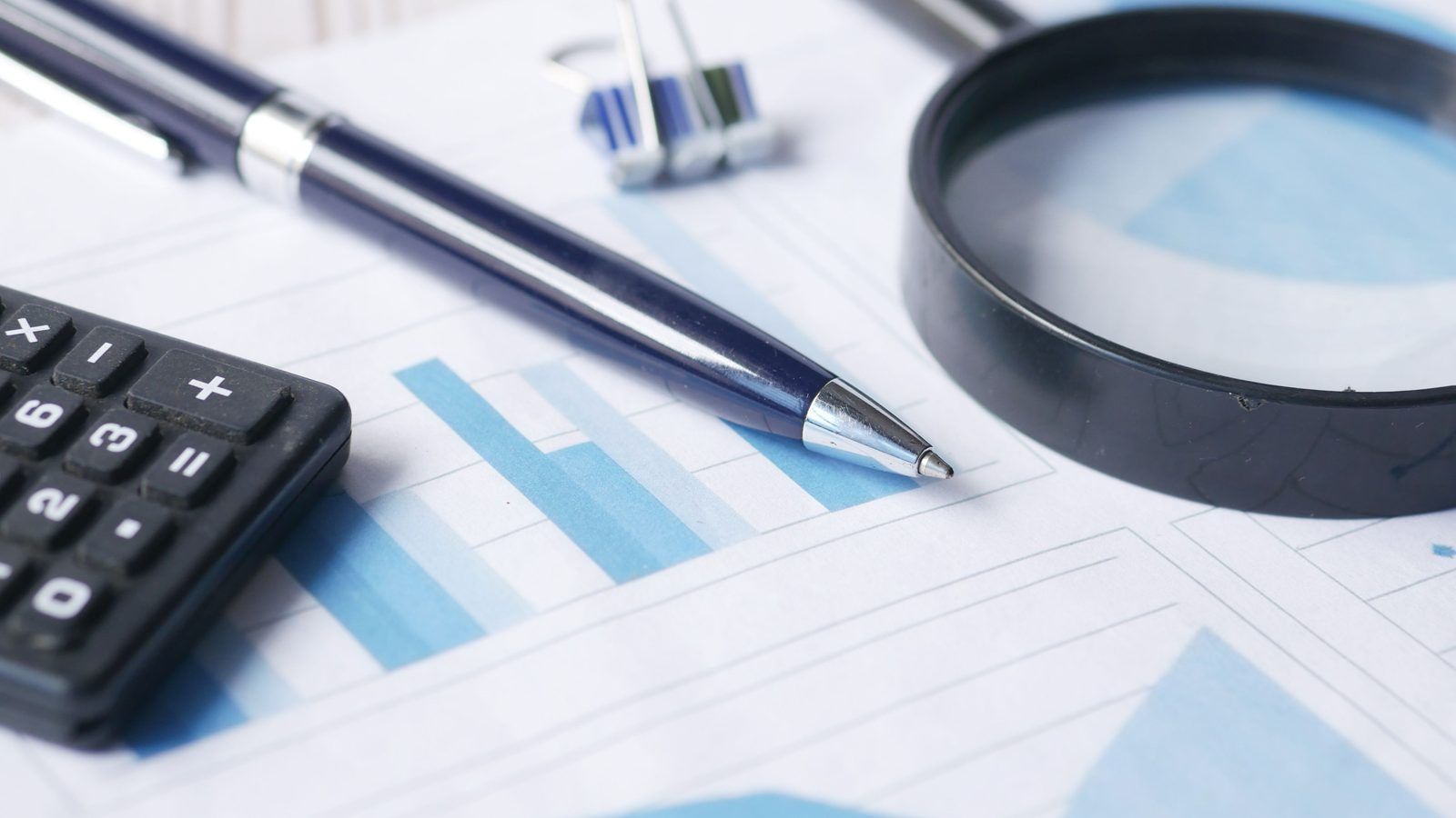 A magnifying glass, calculator, and pen over printed financial documents