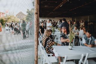 people sitting at white tables in a covered shed