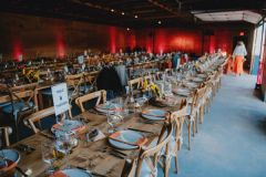 long farm tables set for dinner, orange napkins, sunflower centerpieces, and red uplighting, "Table Thirteen" sign in foreground.