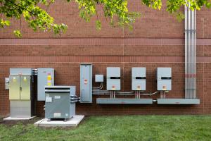 A variety of electrical equipment for the building including inverters, meters, conduit, and breaker box