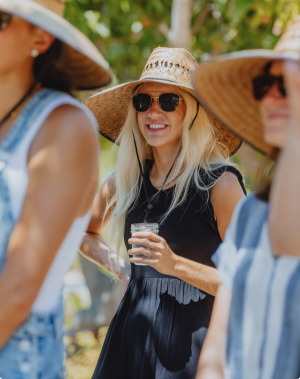 woman smiling holding a drink with a large hat on