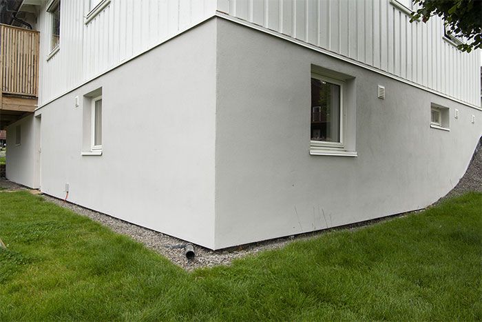 Grunmur på et hvitt hus med en hageflekk foran