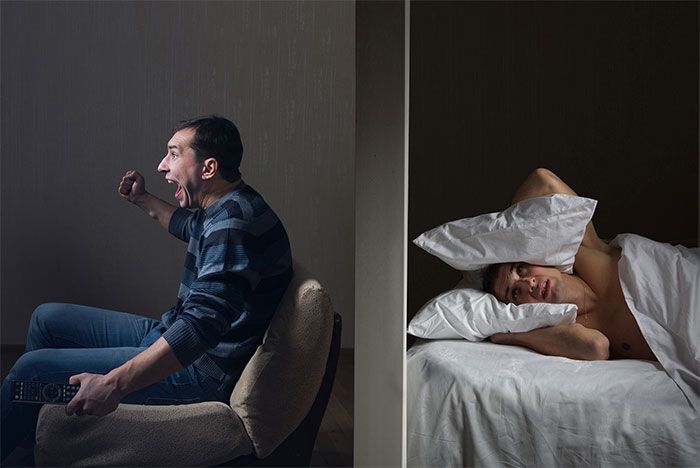 En mann som jubler i sofaen og en dame som holder to puter for ørene