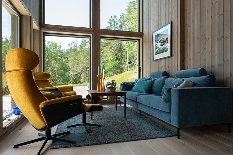 moderne hytte med beiset panel på veggene. Stue med blå sofa og gule lenestoler