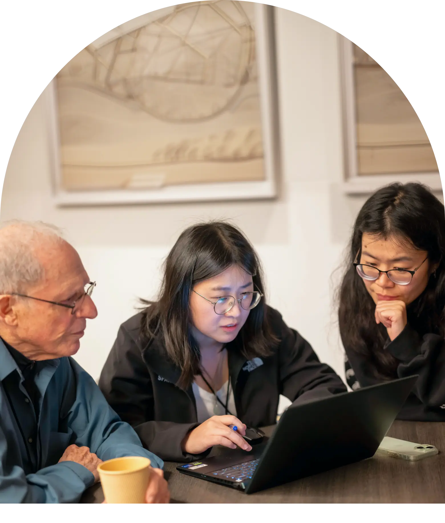 Three colleagues at a meeting table focused on a laptop, one woman pointing at the screen while the others look on.