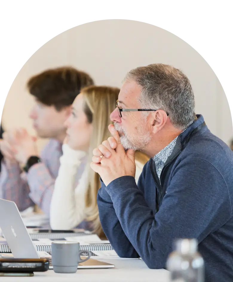 Attendees of a seminar sit at a table, looking focused and thoughtful