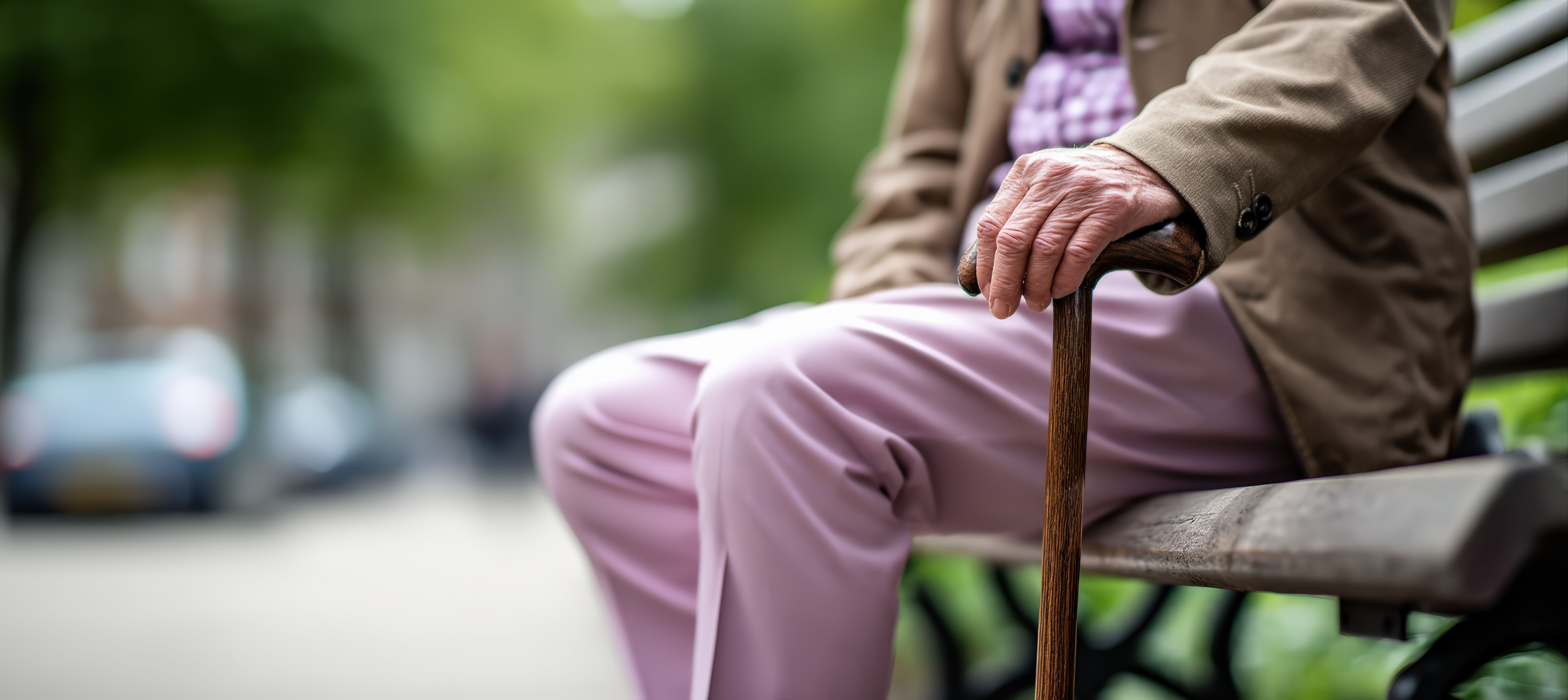 Senior person's hand holding a walking cane while sitting on a park bench