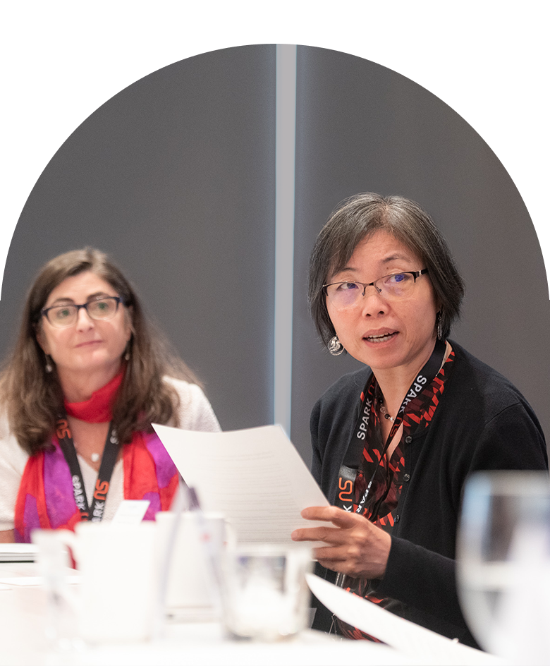 Attendees of a seminar sit at a table, looking focused and thoughtful