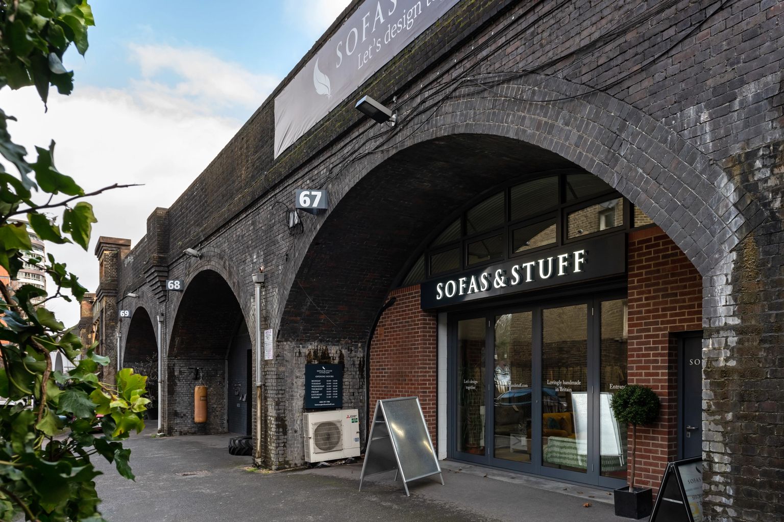A Sofas & Stuff store occupies a dark brick railway arch, with more arches extending down a street.