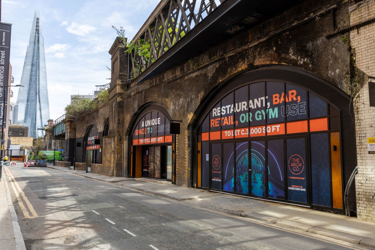 Street with brick railway arches advertising spaces for rent, with The Shard skyscraper in the background.