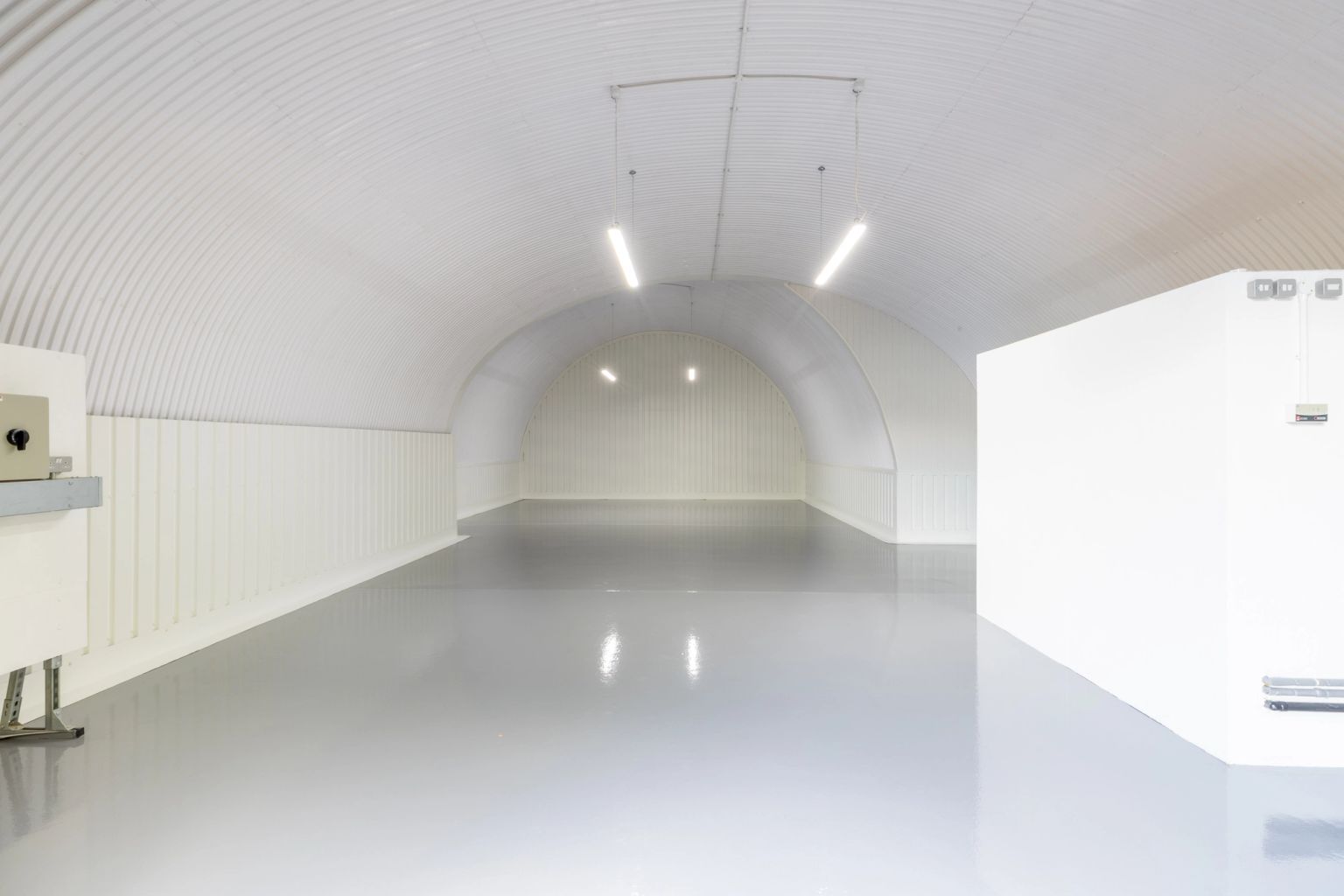 Empty, clean, white arched space with corrugated ceiling and reflective grey floor.