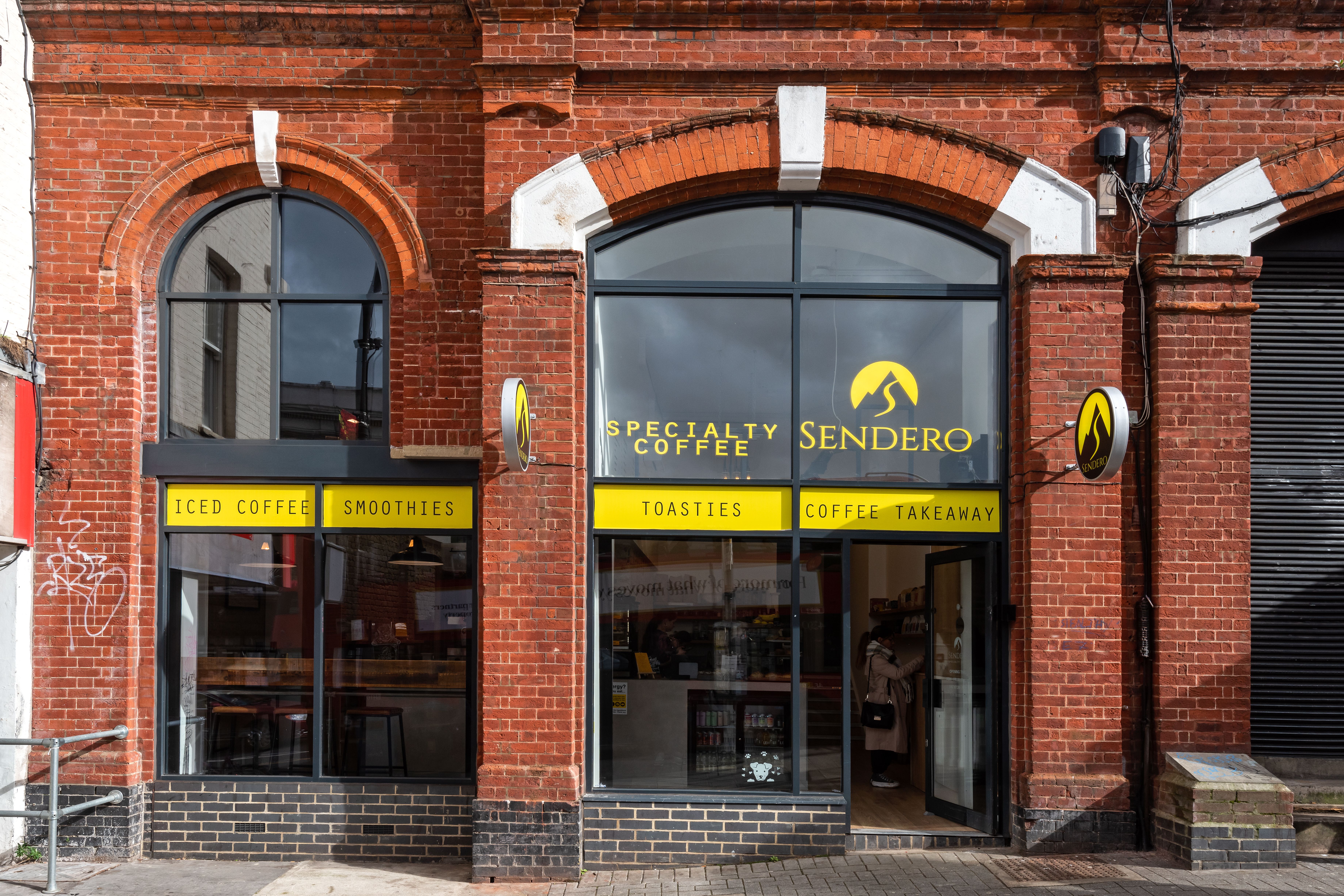 Sendero Specialty Coffee shop in a red brick building with arched windows and yellow signs.