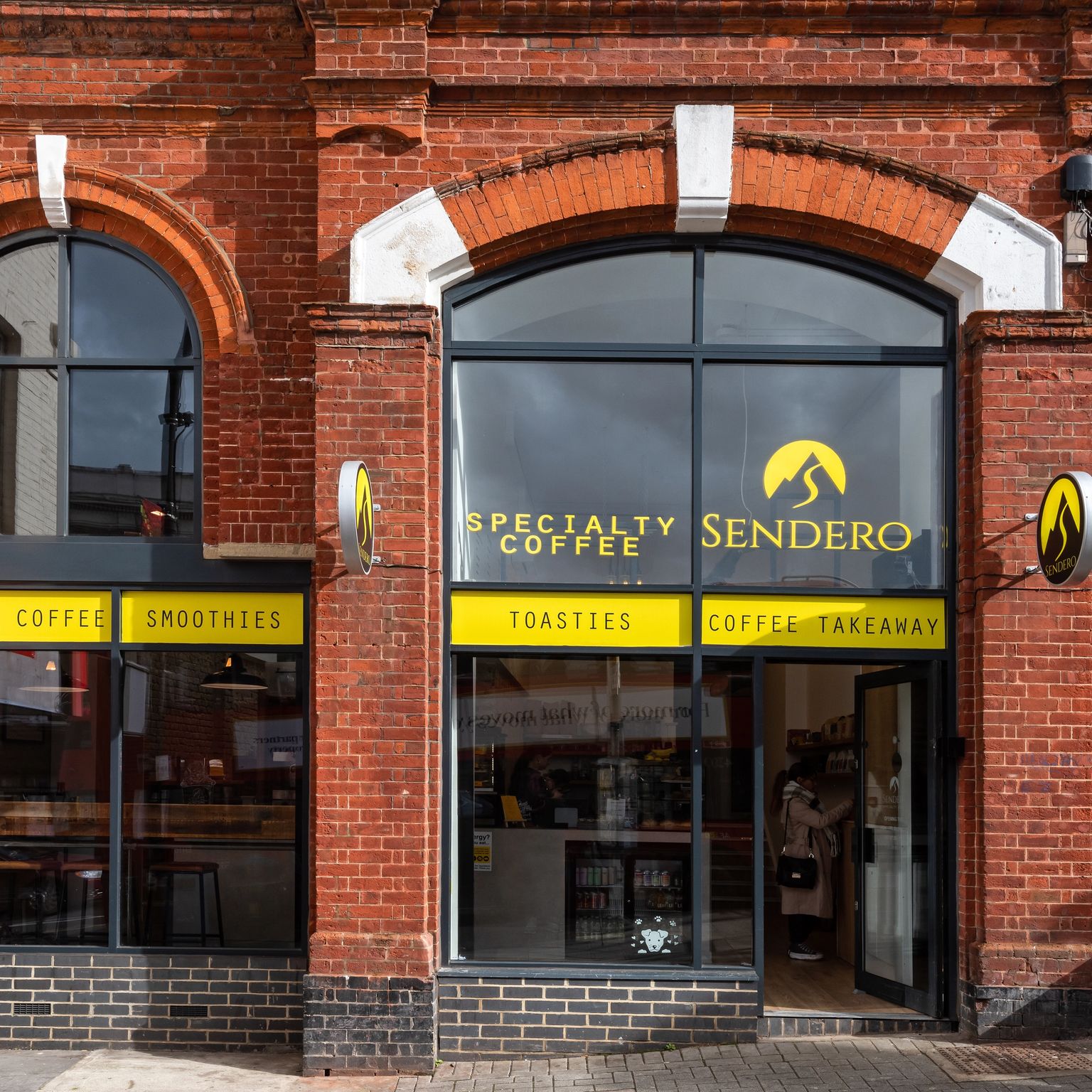 Sendero Specialty Coffee shop in a red brick building with arched windows and yellow signs.