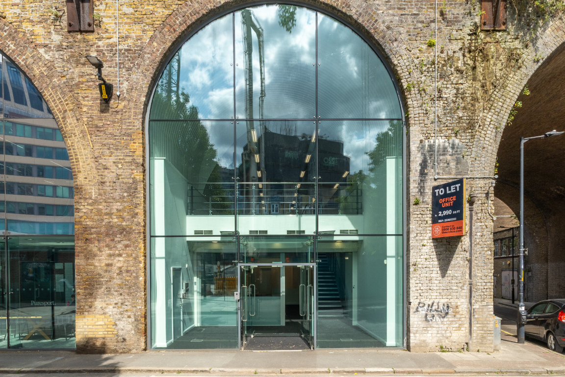 Modern glass facade built into a brick archway, with a 'To Let' sign.