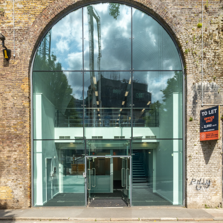 Modern glass facade built into a brick archway, with a 'To Let' sign.