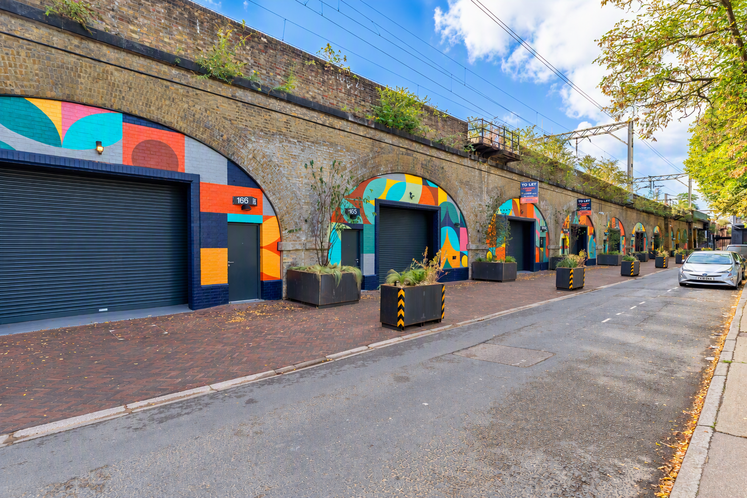 Railway arches painted with colorful geometric murals along a street.