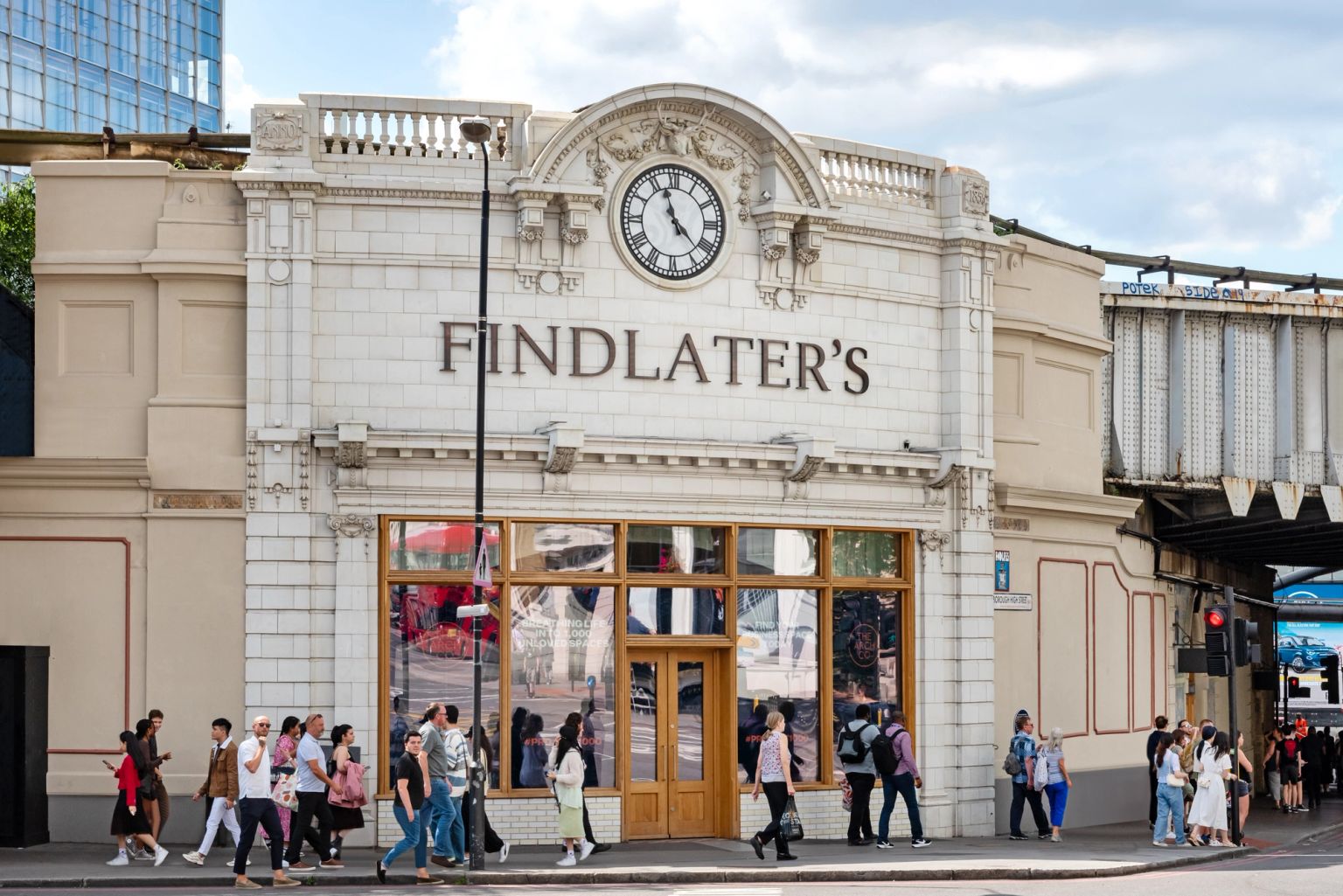 A white building with "Findlater's" and a clock, pedestrians on the sidewalk, and a railway bridge.