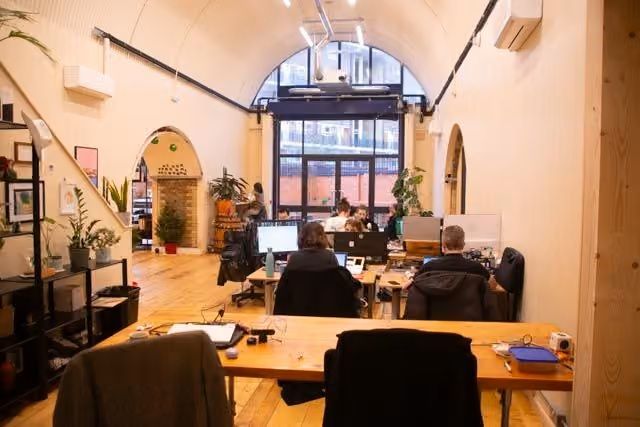 Open-plan office with an arched ceiling, large windows, and several people working at computers.