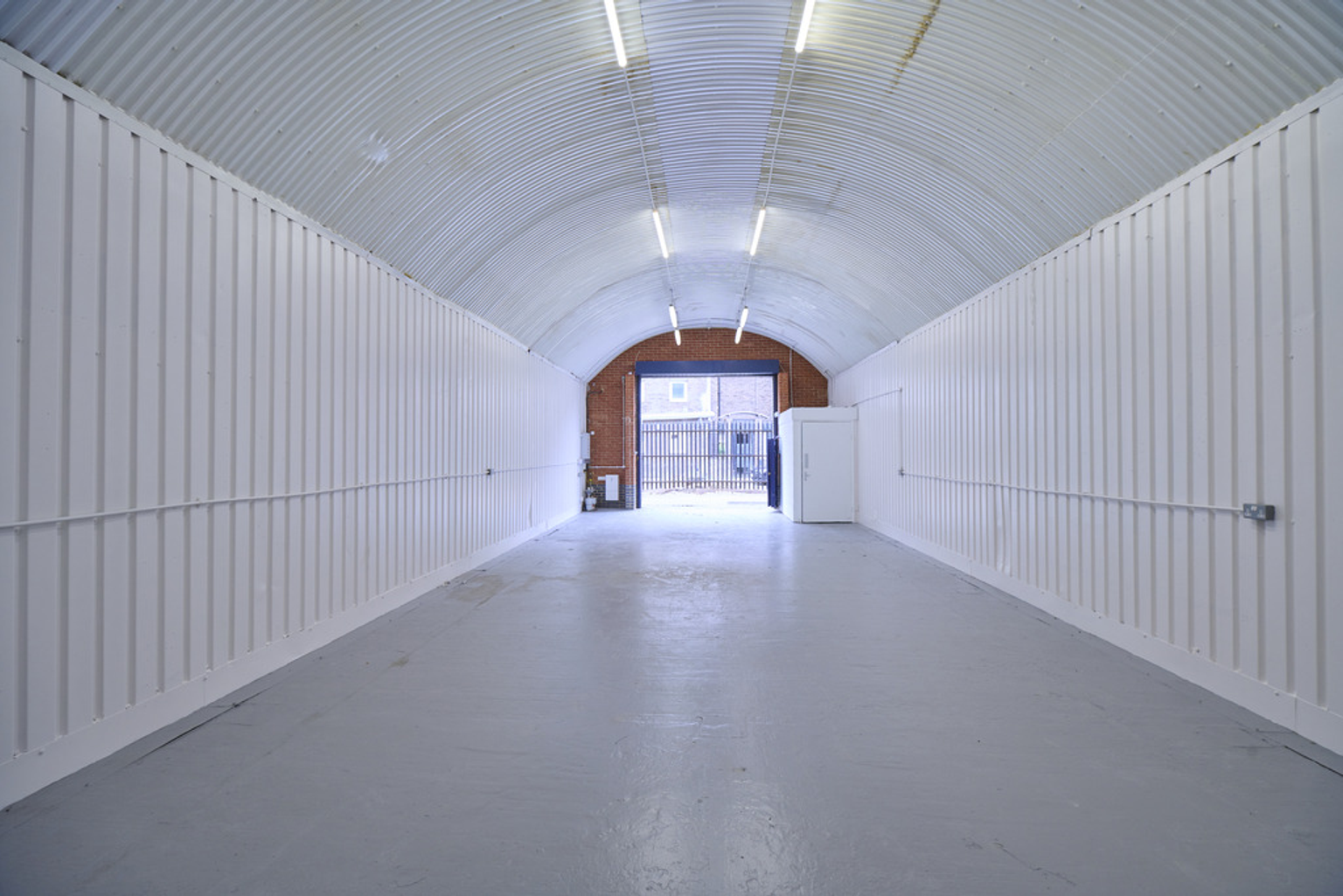 An empty arch with white lining, facing the front electric roller shutter entrance, which is open.