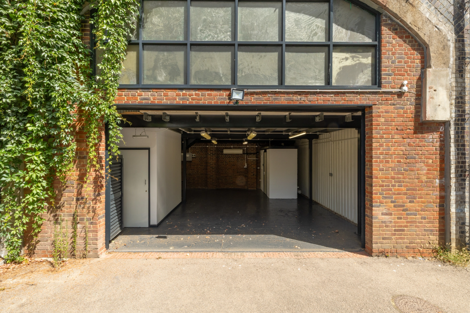 The front of an arch, with high level glazing, and an open electric roller shutter entrance big enough for vehicle access.