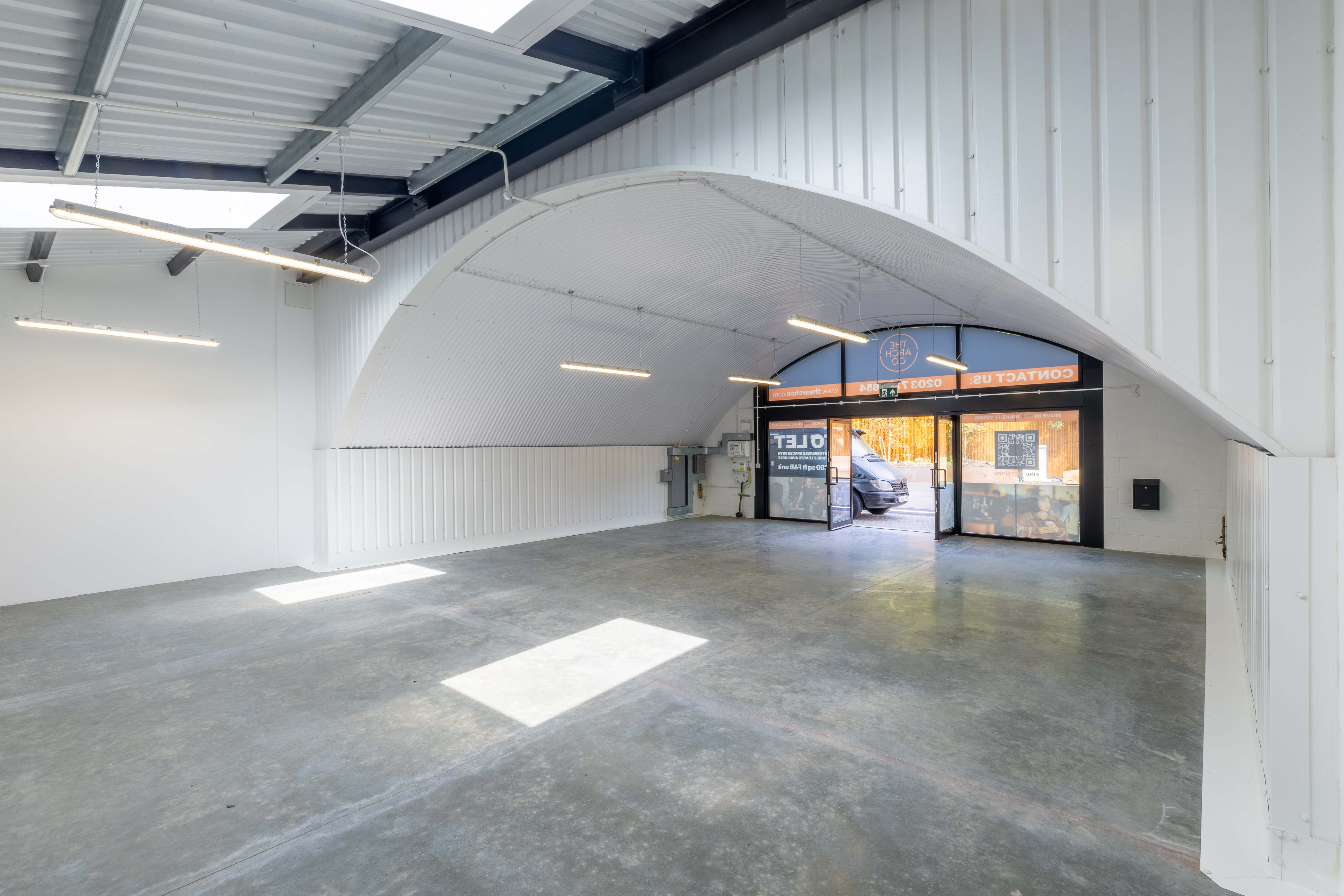 An empty, modern commercial space with a concrete floor, white walls, and an arched entrance with glass doors.