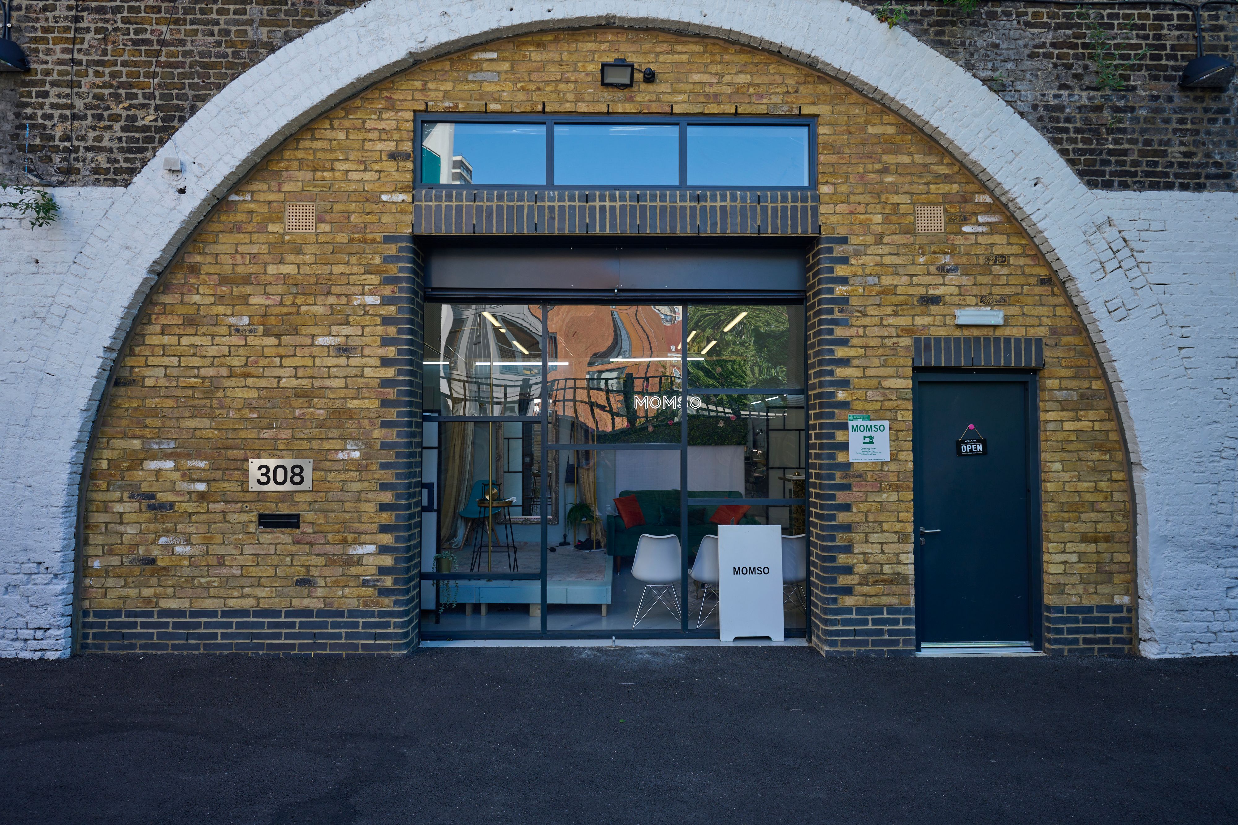 A modern furniture store named MOMSO in a yellow brick archway, with address number 308, large glass windows, and a dark blue door.