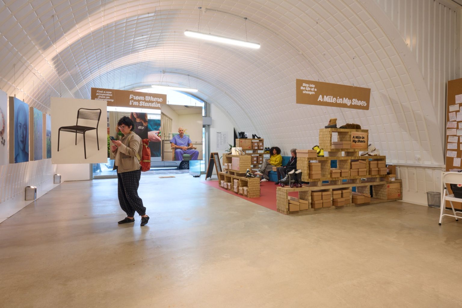 An exhibition hall with an arched ceiling, featuring art displays and a shoe exhibition labeled "A Mile in My Shoes."