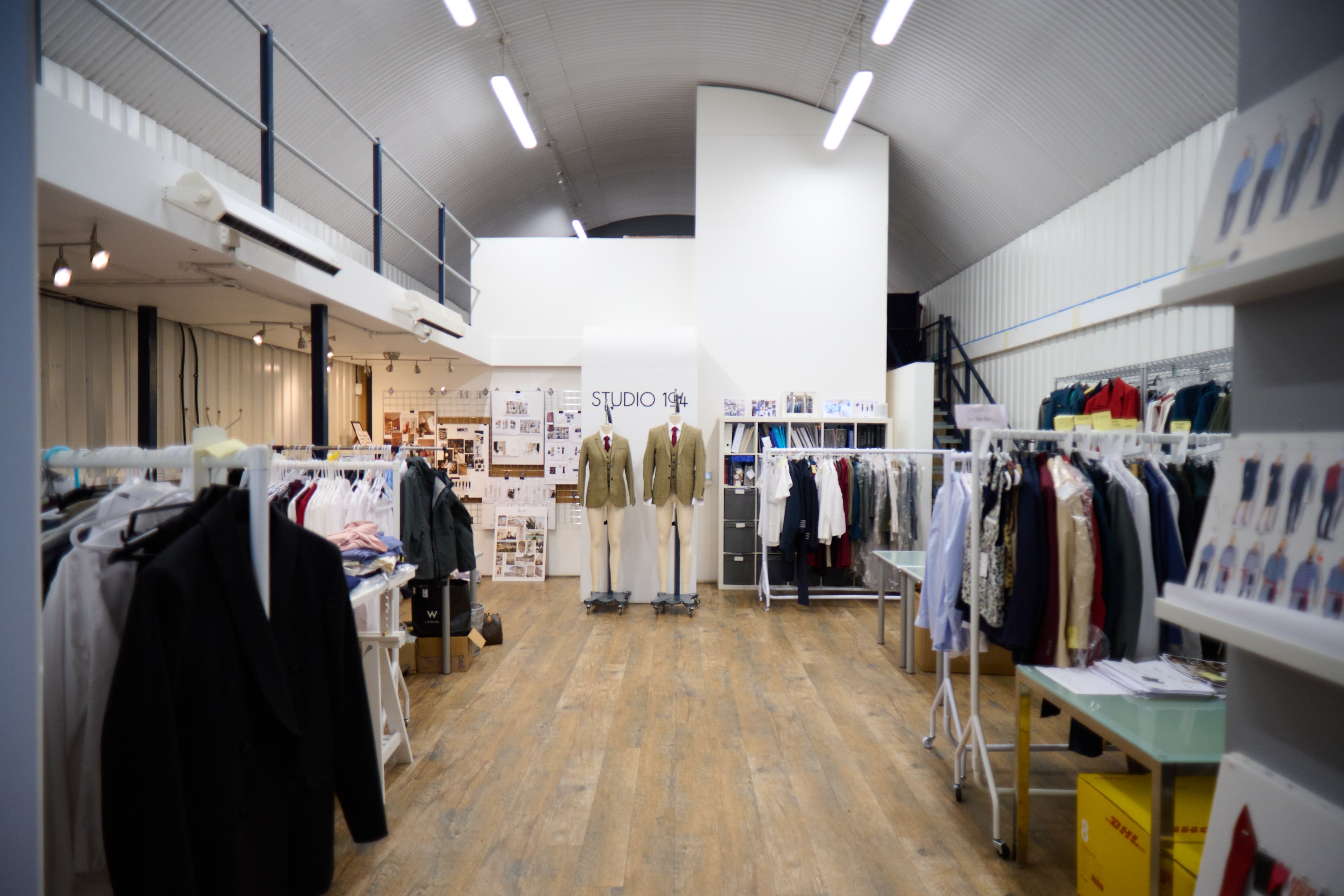 Clothing design studio interior with garment racks, two mannequins wearing jackets, and a "STUDIO 104" sign.