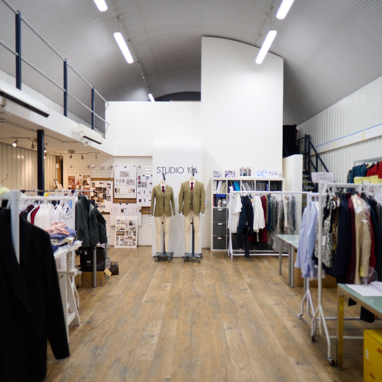 Clothing design studio interior with garment racks, two mannequins wearing jackets, and a "STUDIO 104" sign.