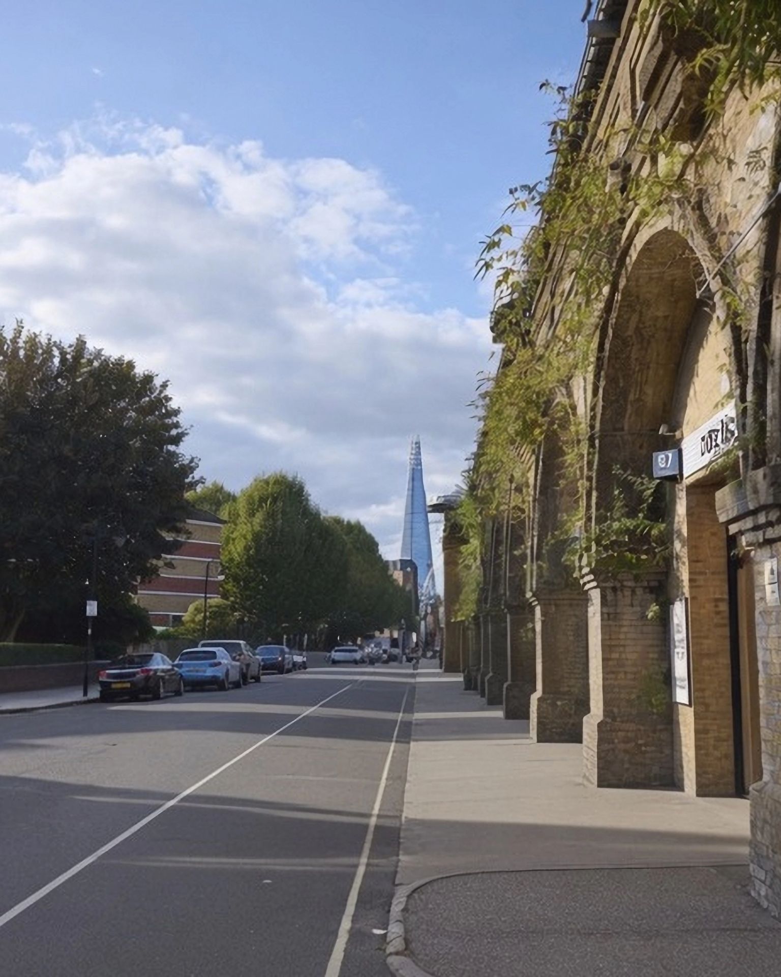A street lined with brick railway arches on the right and buildings on the left, with The Shard skyscraper visible in the distance.