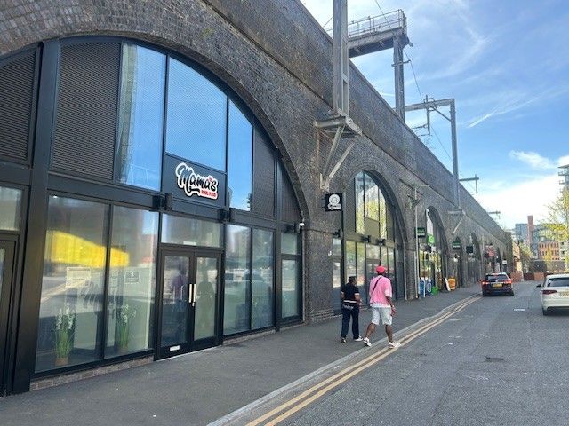 A row of brick railway arches converted into businesses, including "Mama's Delicious Dumplings," with people walking on the sidewalk.
