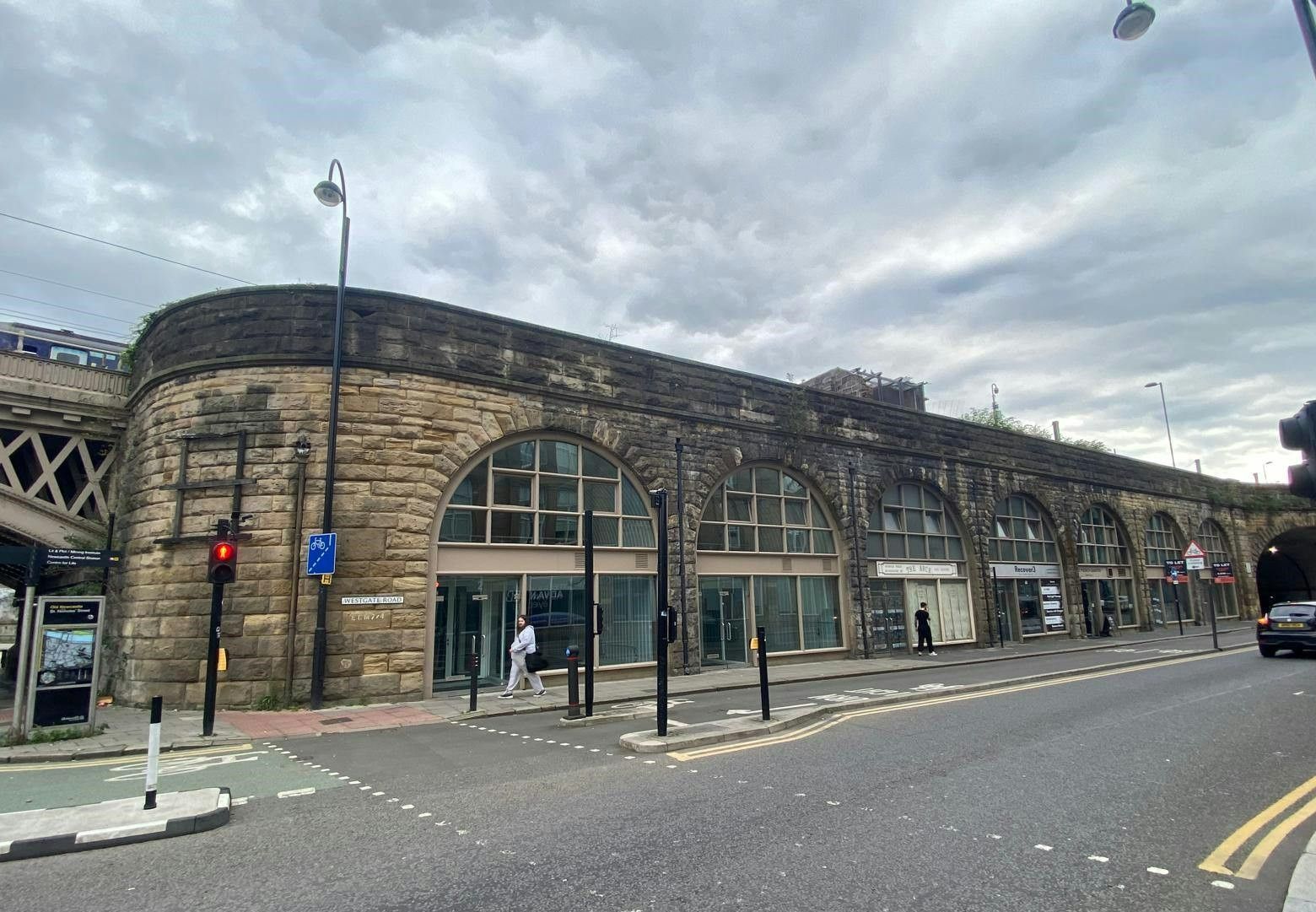 Stone railway arches converted into shops lining a street under an overcast sky.
